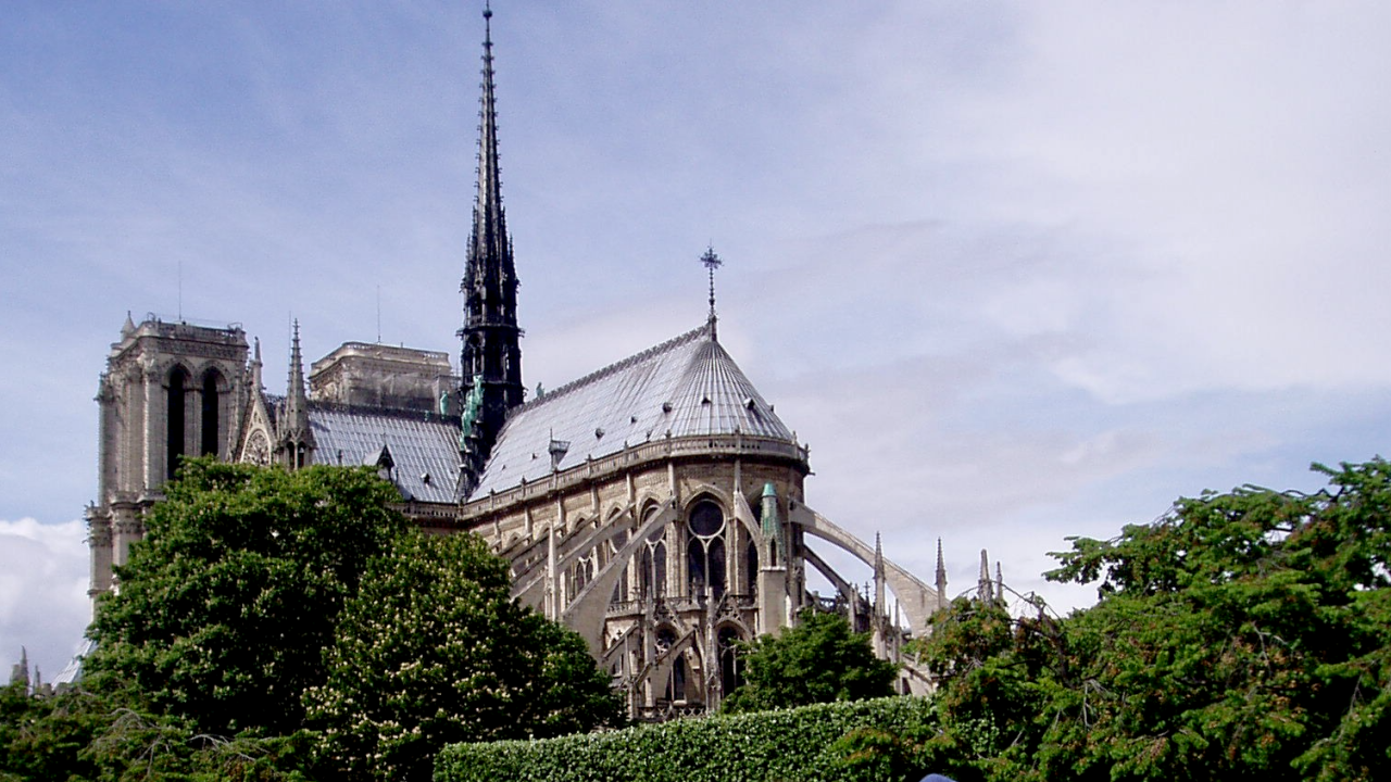 A long-range view of Notre Dame cathedral with flying buttresses and trees on either side.